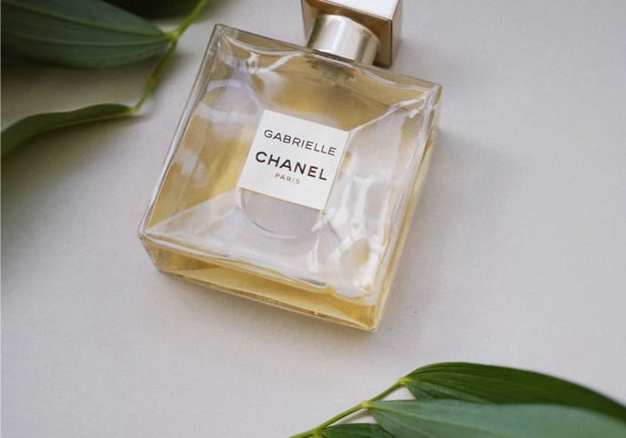 Chanel parfum bottle on a white background surrounded by green leaves